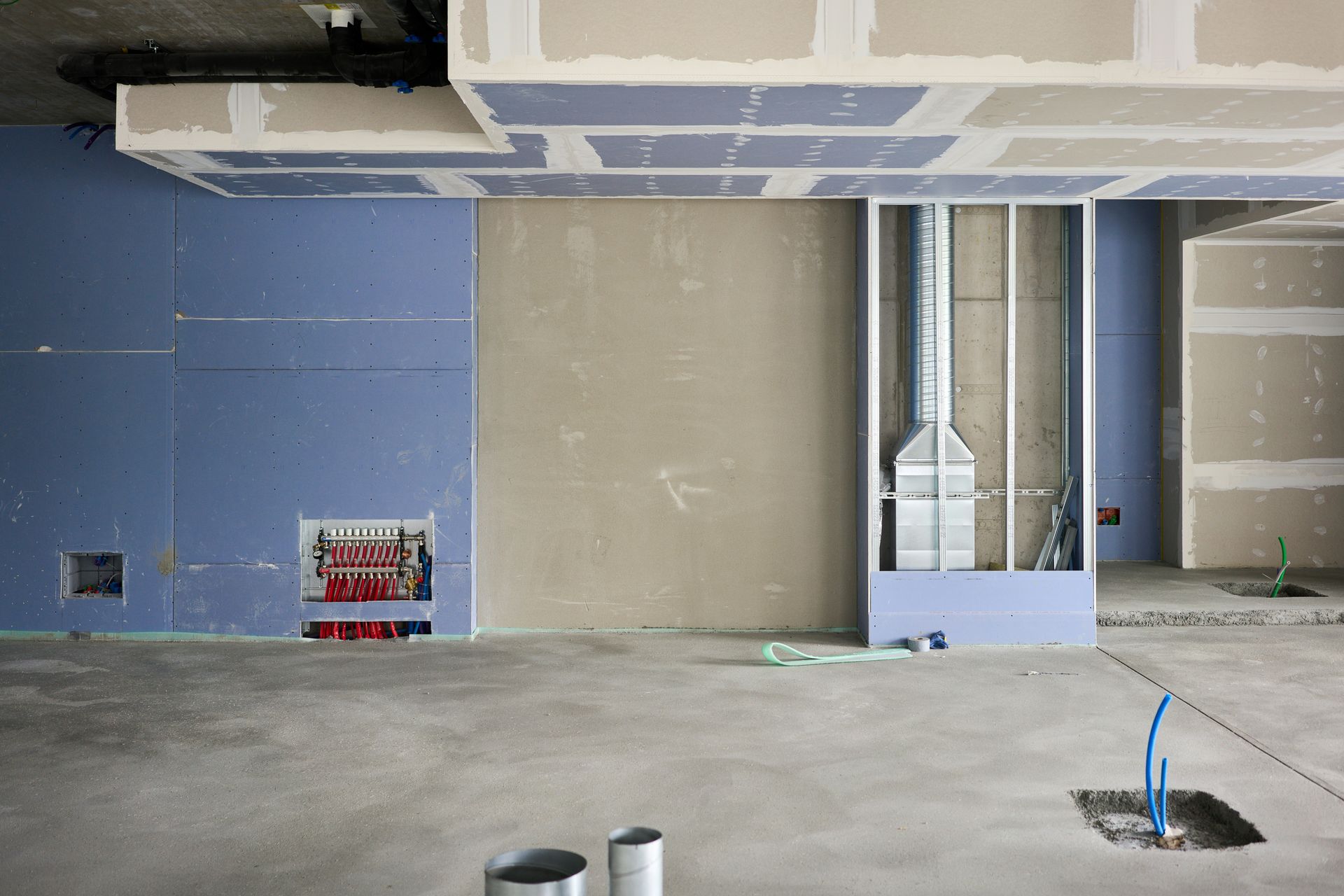 Unfinished interior with exposed ductwork, blue and beige walls, and construction materials on the floor