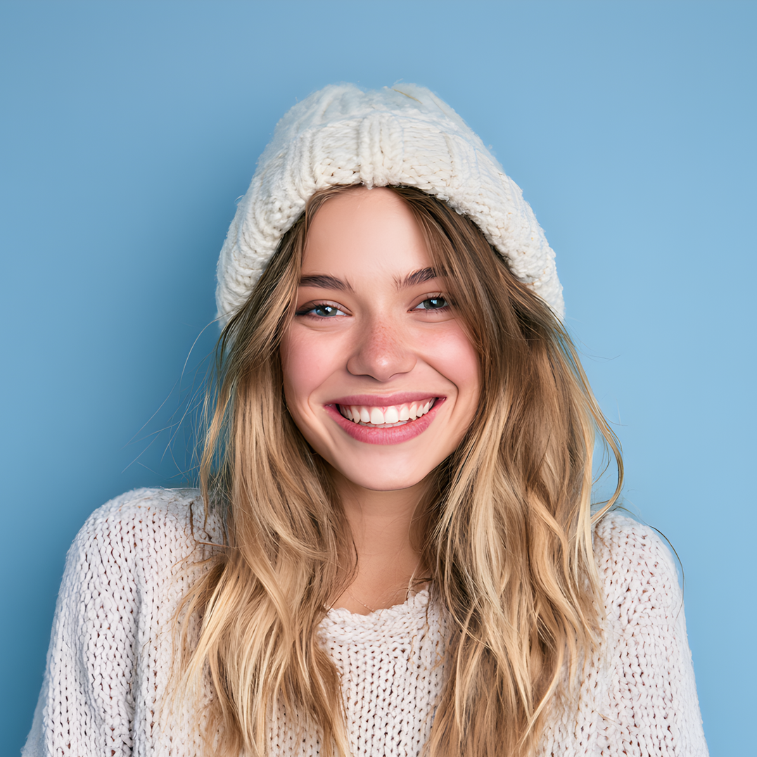 Smiling person in a white knit hat and sweater against a blue background