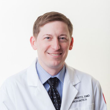 Smiling doctor in a white coat and tie against a plain white background