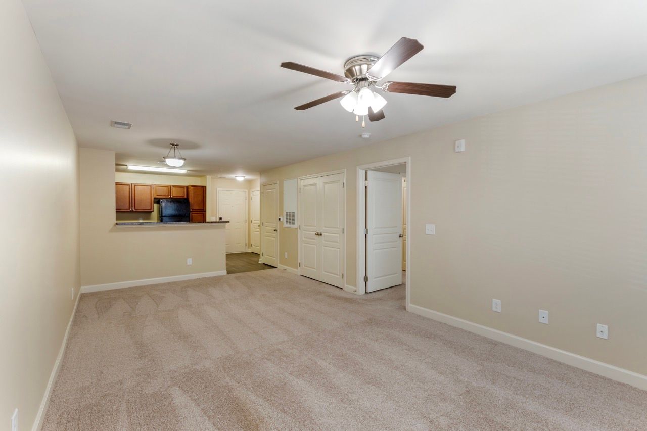 Open-concept living area with ceiling fan, beige walls, and kitchen pass-through.