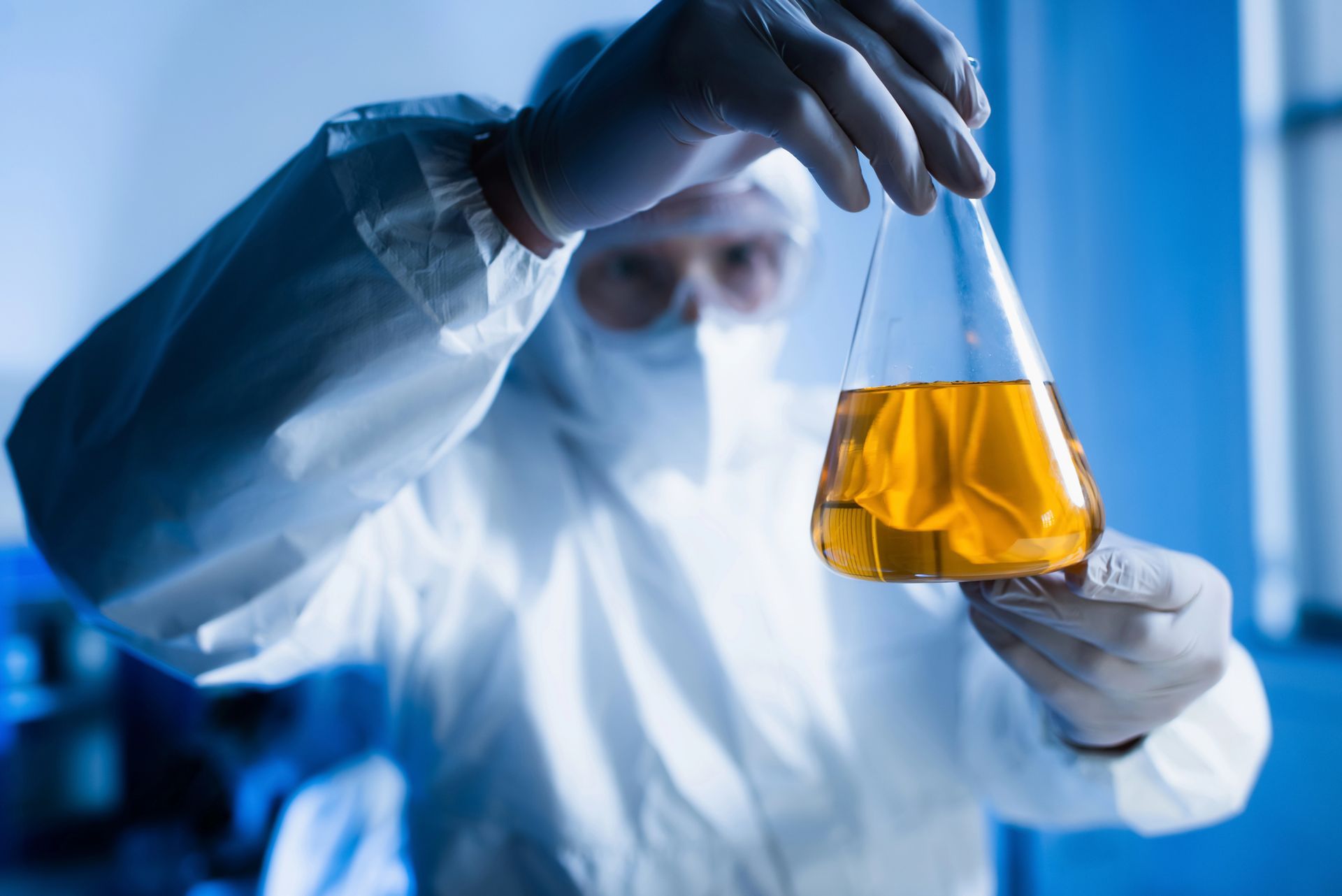Scienziato in tuta protettiva che tiene in mano una fiaschetta contenente un liquido giallo in un laboratorio