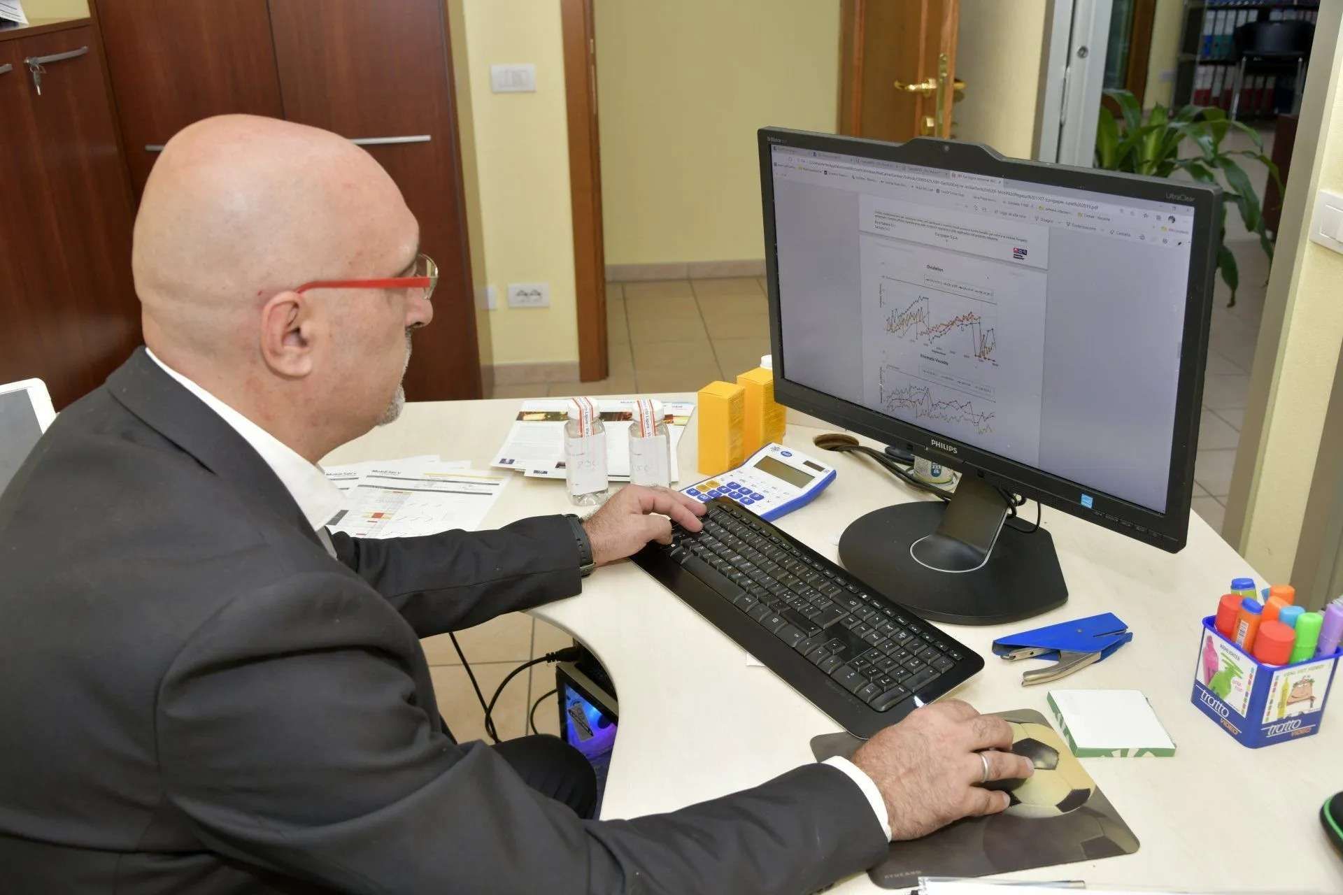 Un uomo in giacca e cravatta usa un computer fisso a una scrivania in ufficio.