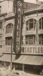 Vintage, sepia-toned street view of the Sattler’s department store building featuring a large, vertical, neon sign.