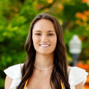 A woman wearing a white top and a yellow sash is smiling for the camera.