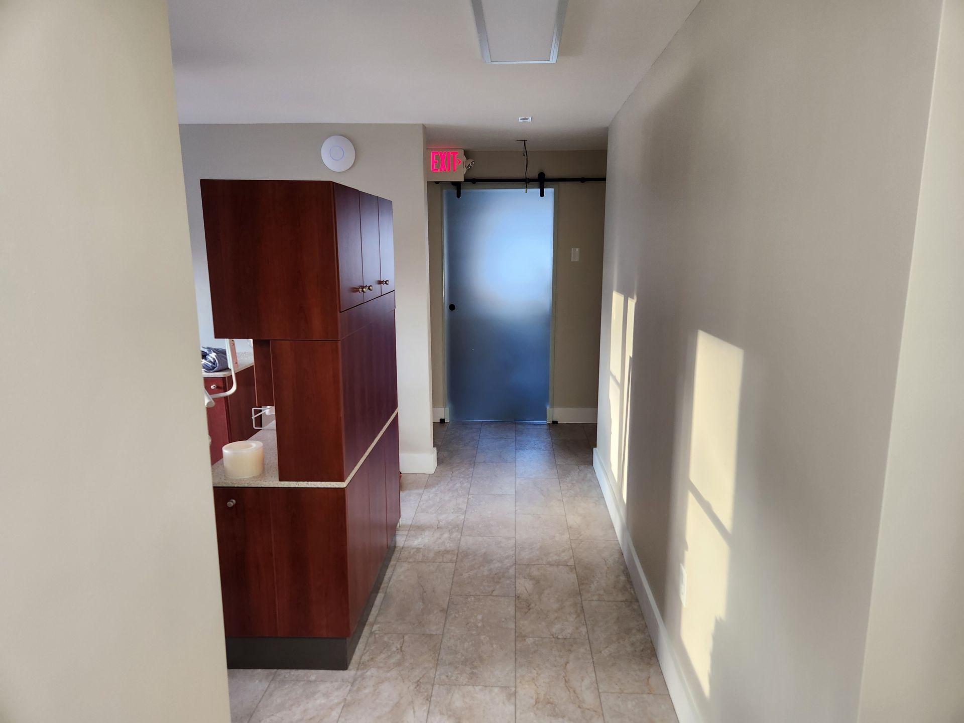 A hallway in a dental office with a red exit sign.