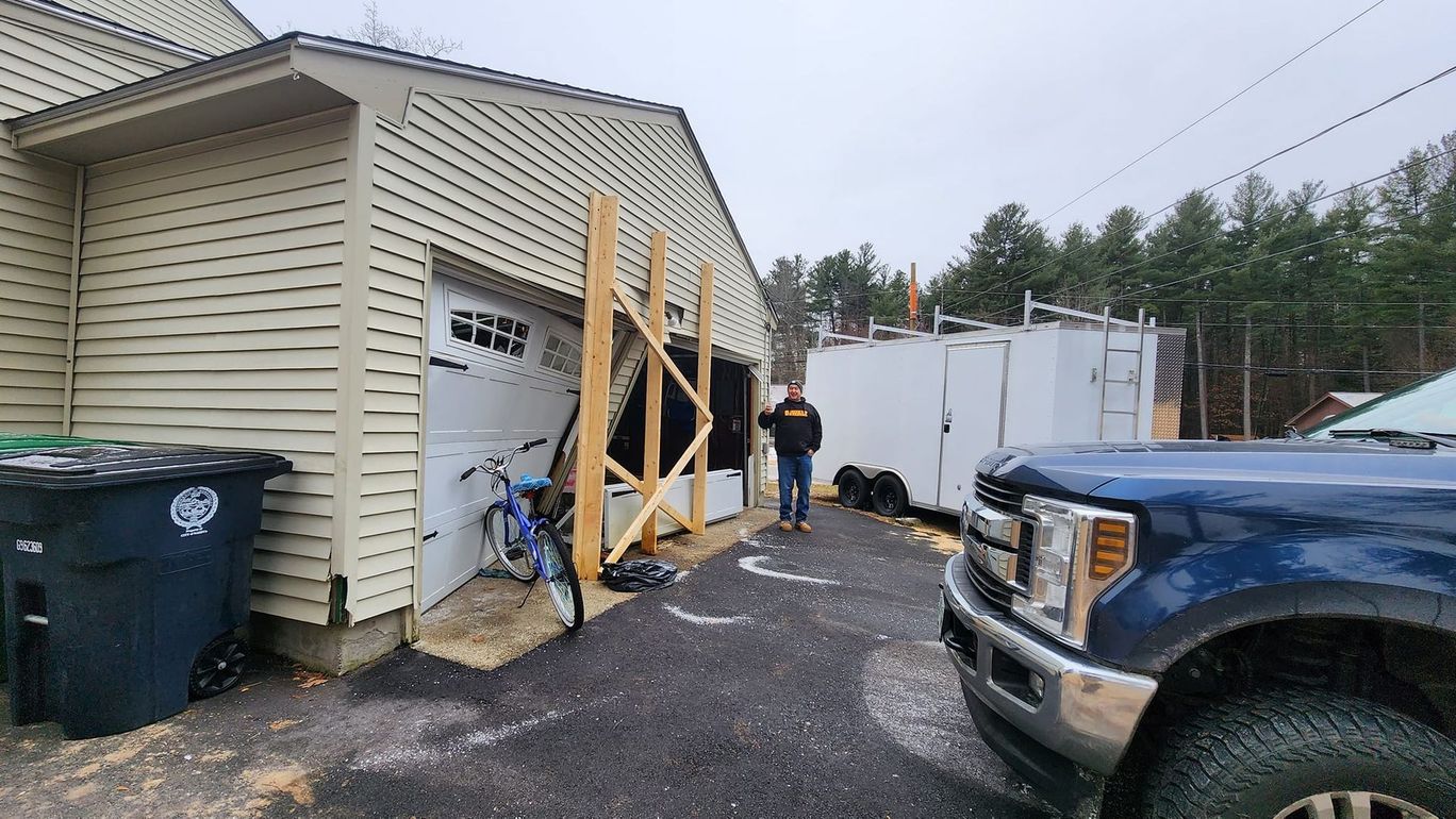 A man is standing in front of a garage next to a truck.