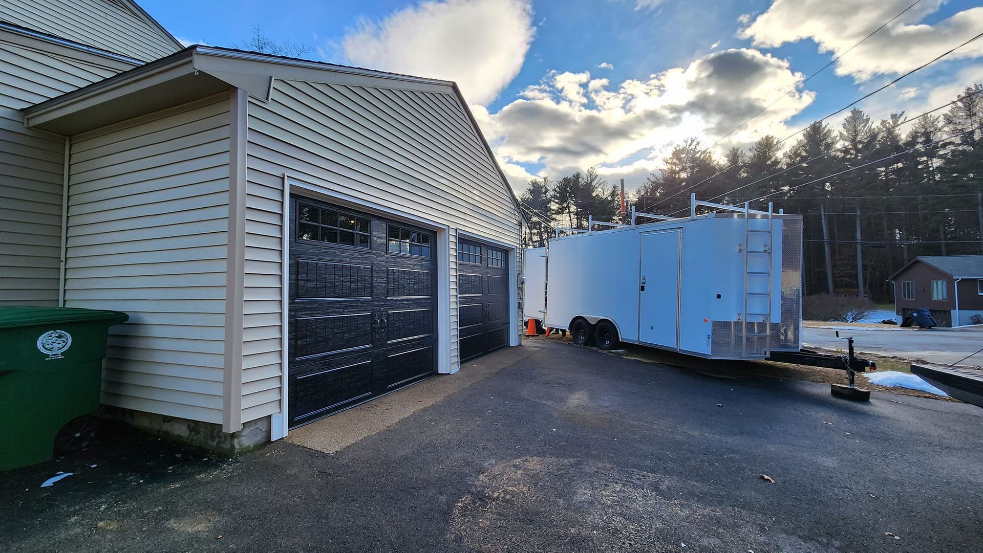A white trailer is parked in front of a garage.