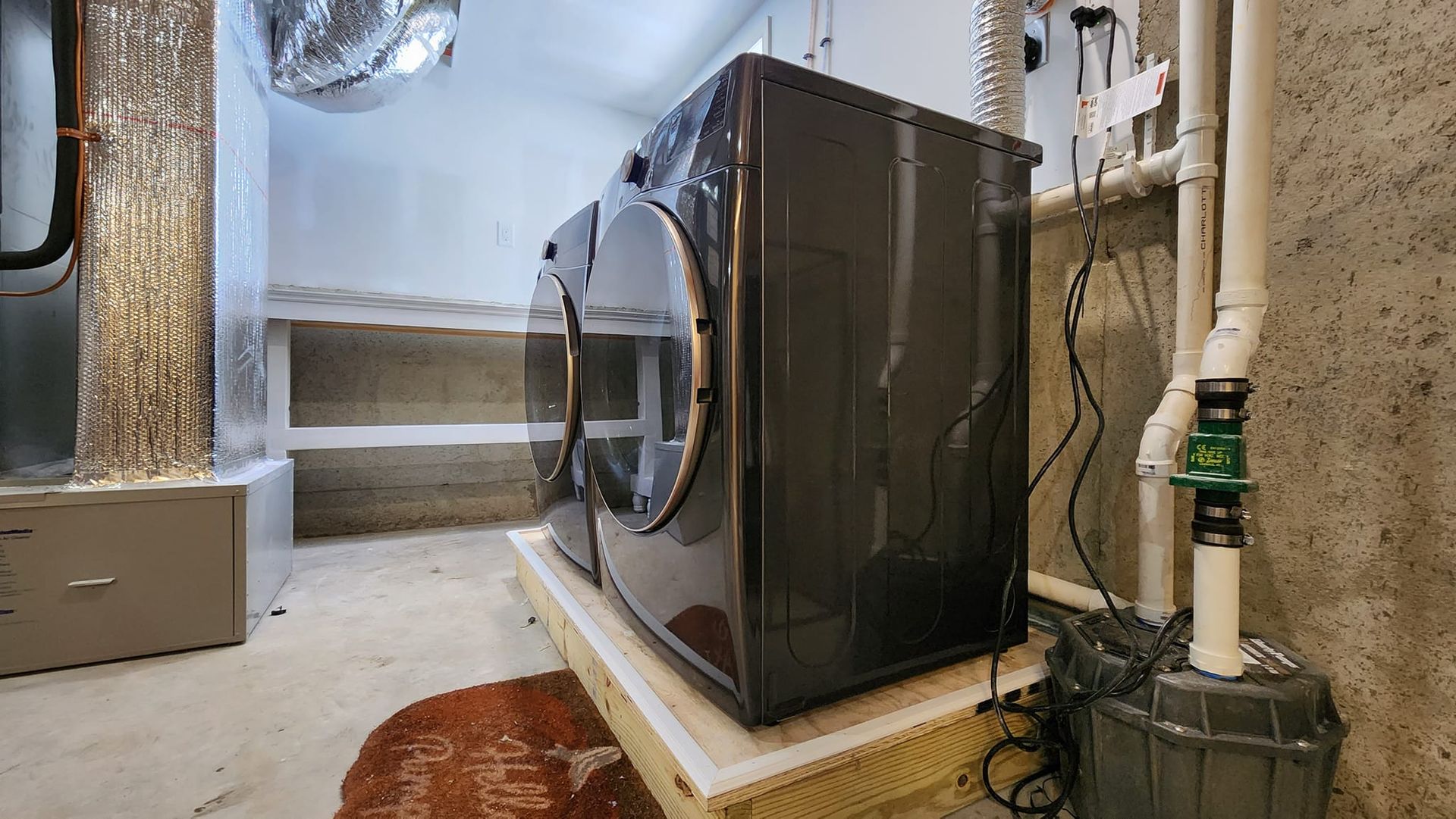A washer and dryer are sitting on a wooden platform in a basement.