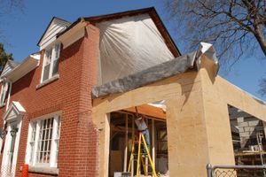 A man is standing on a ladder in front of a house under construction