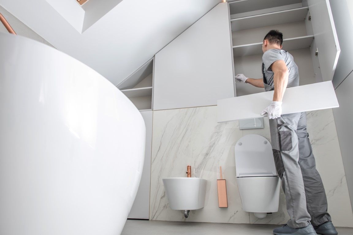Contractor installing custom cabinetry in a modern bathroom with marble walls, a freestanding bathtub, and sleek fixtures.