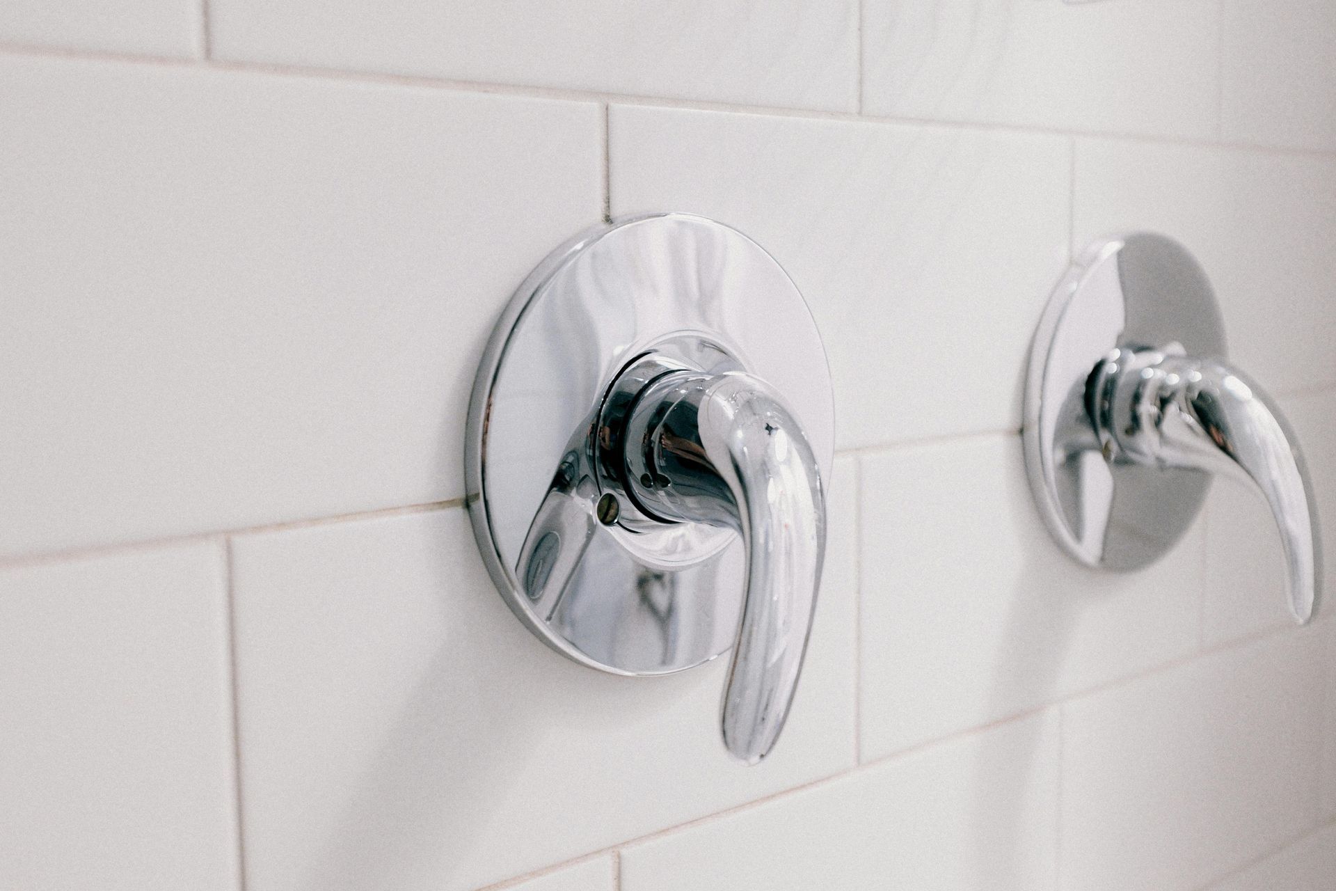 White ceramic wall surface with chrome shower handles mounted above clean horizontal grout lines.