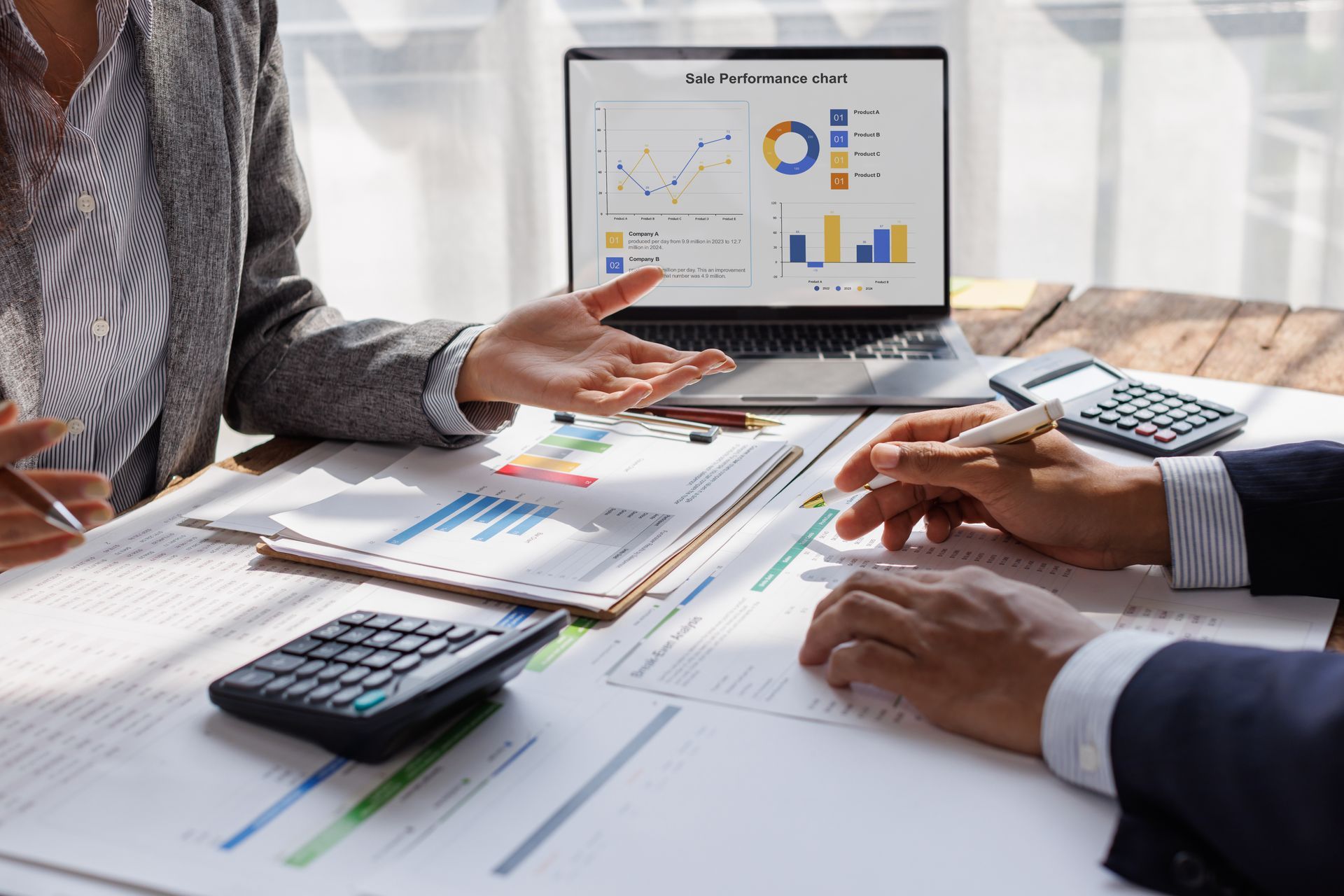 Two people reviewing financial reports with a laptop displaying charts and graphs, and two calculators Two people reviewing financial reports with a laptop displaying charts and graphs, and two calculators