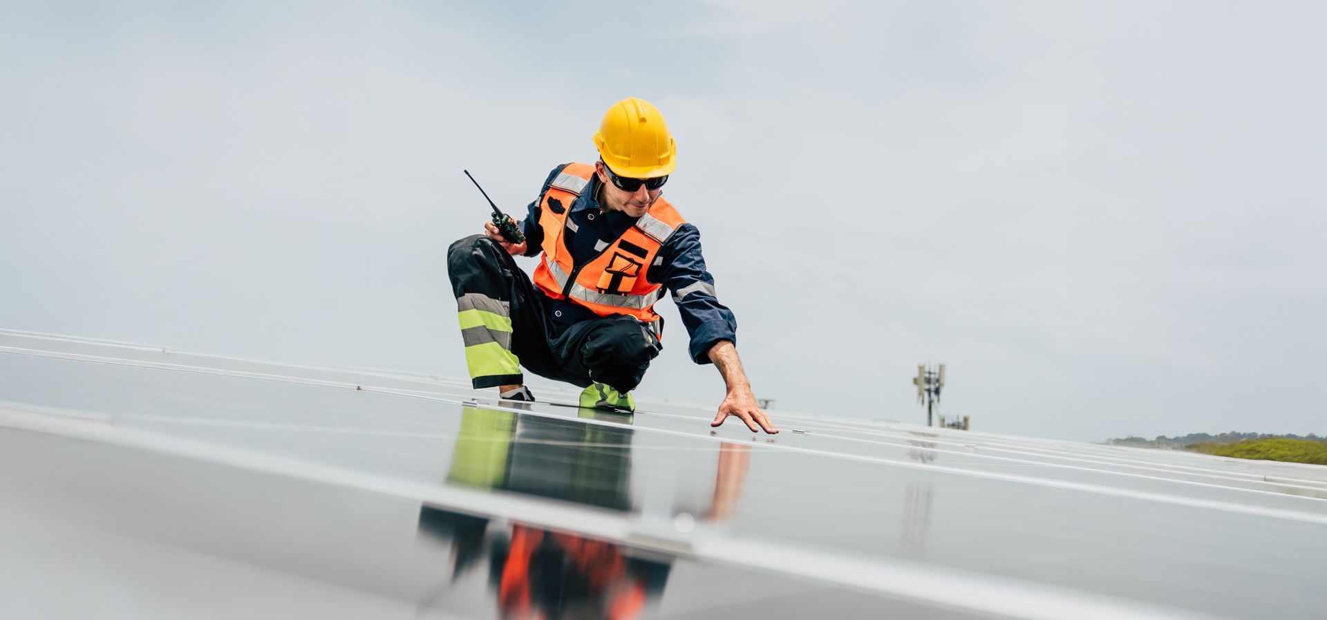 A worker in safety gear inspects solar panels on a rooftop A worker in safety gear inspects solar panels on a rooftop