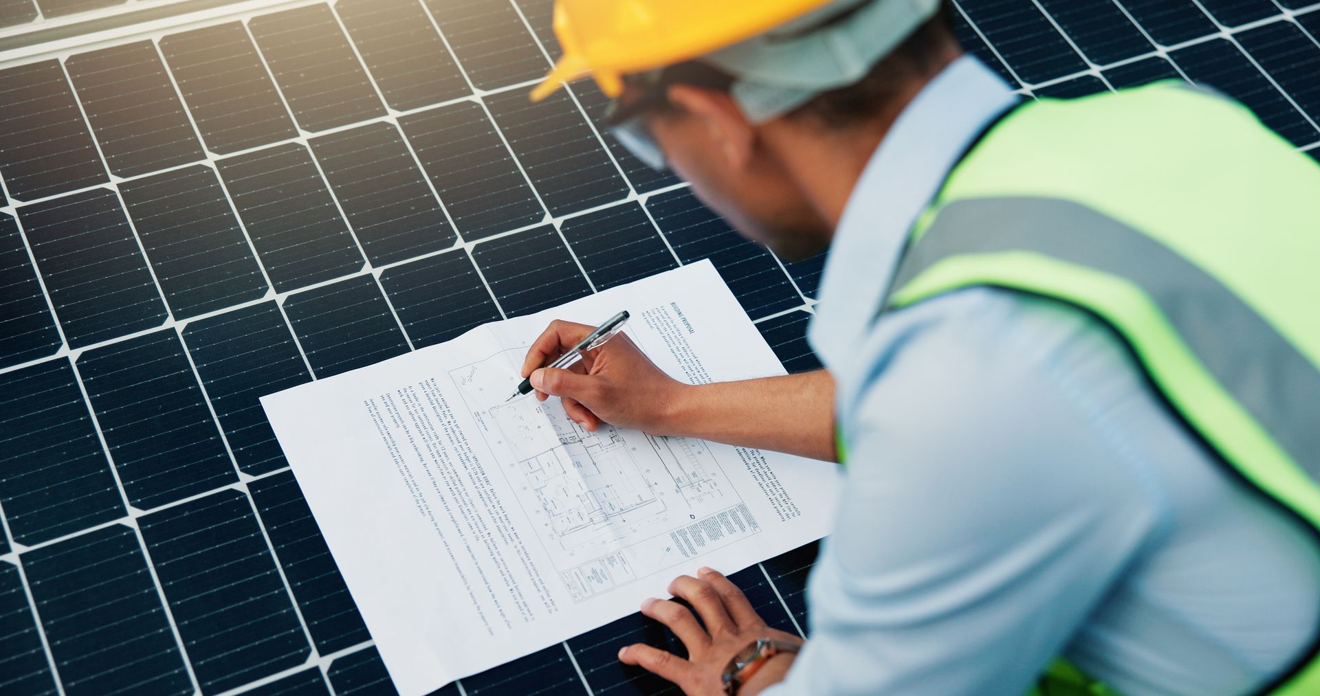 Person in hardhat and vest, inspecting solar panels, taking notes on a document Person in hardhat and vest, inspecting solar panels, taking notes on a document