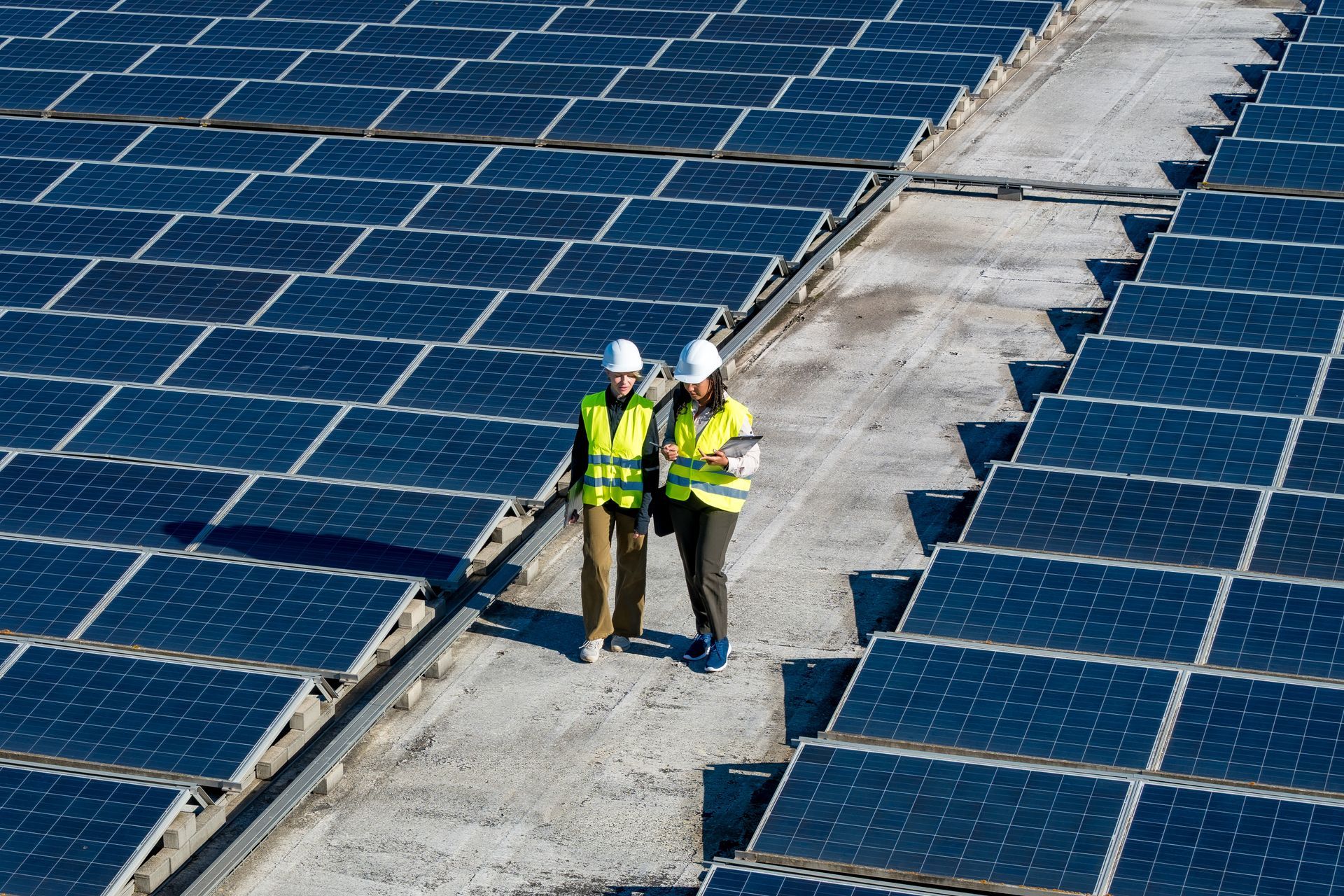 Two people in safety vests and hard hats on a rooftop solar panel array Two people in safety vests and hard hats on a rooftop solar panel array