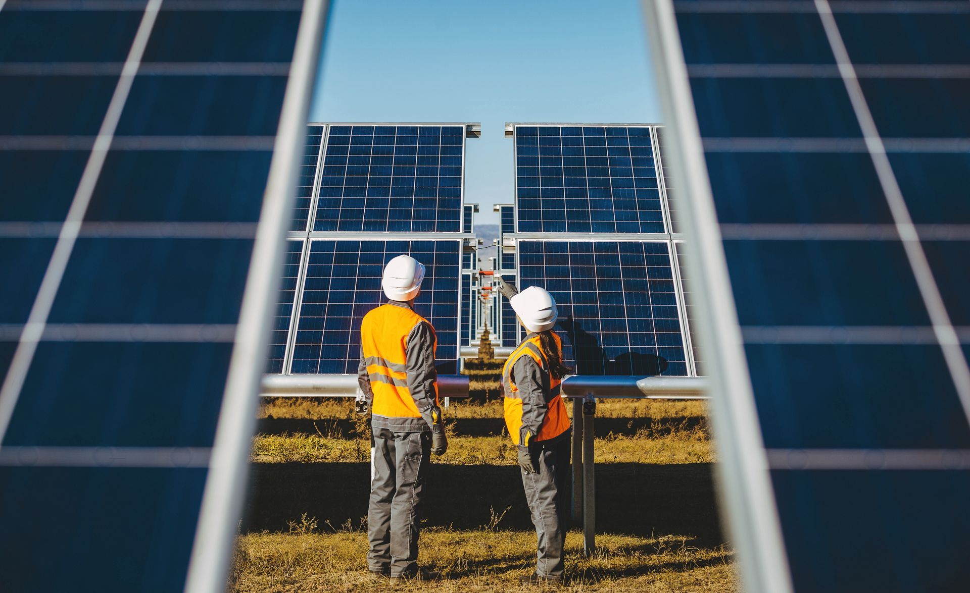 Two workers in safety vests and helmets inspecting solar panels in a field