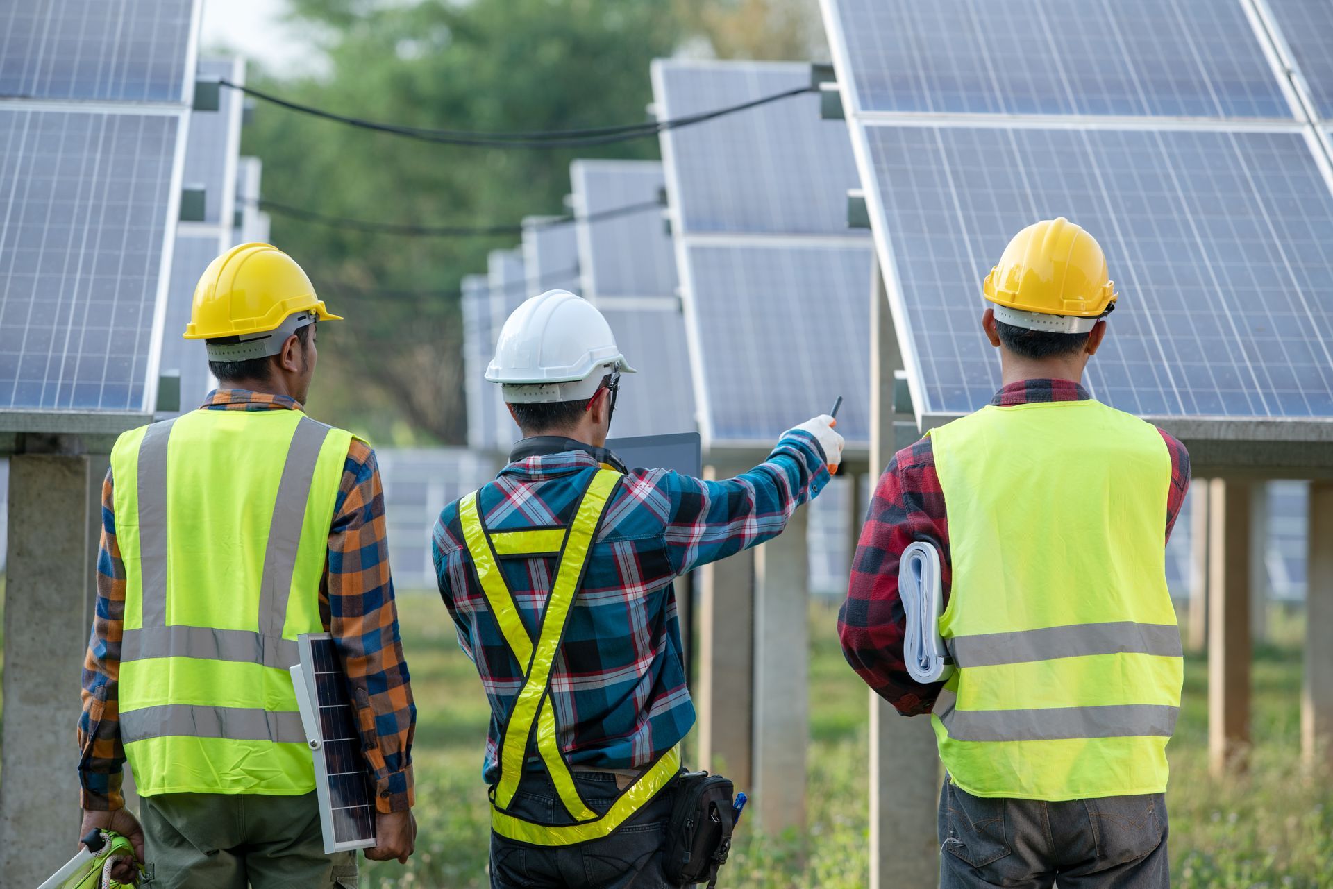 Three workers in safety vests and helmets inspect solar panels Three workers in safety vests and helmets inspect solar panels