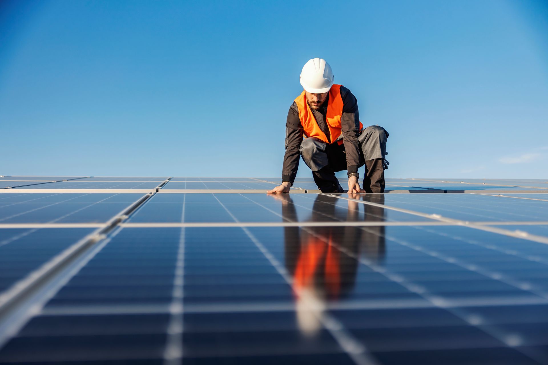Worker in safety gear inspecting solar panels on a rooftop against a blue sky