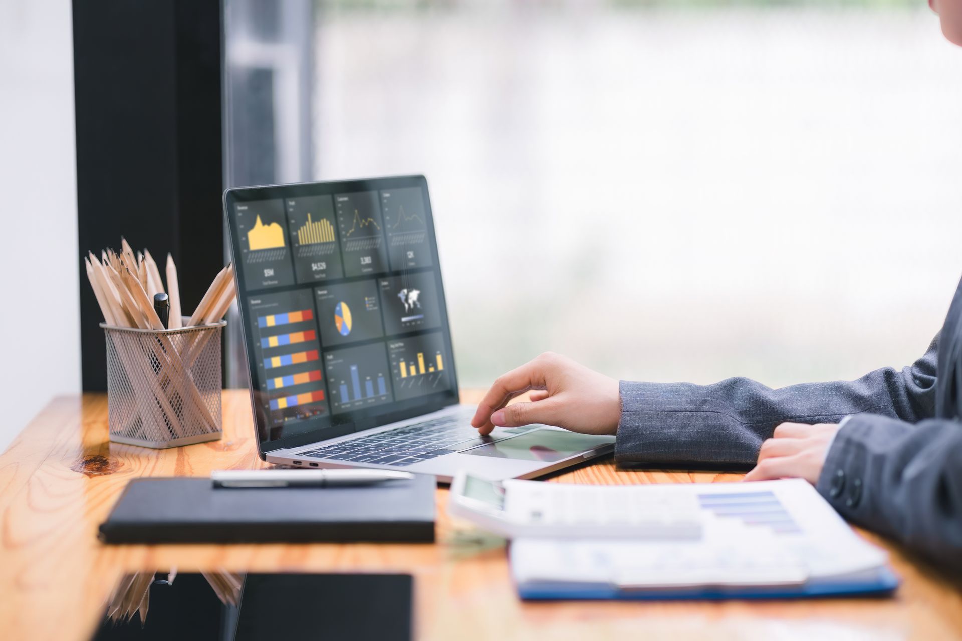 Person using a laptop displaying financial charts and data, with papers, calculator, and pencils on a desk Person using a laptop displaying financial charts and data, with papers, calculator, and pencils on a desk
