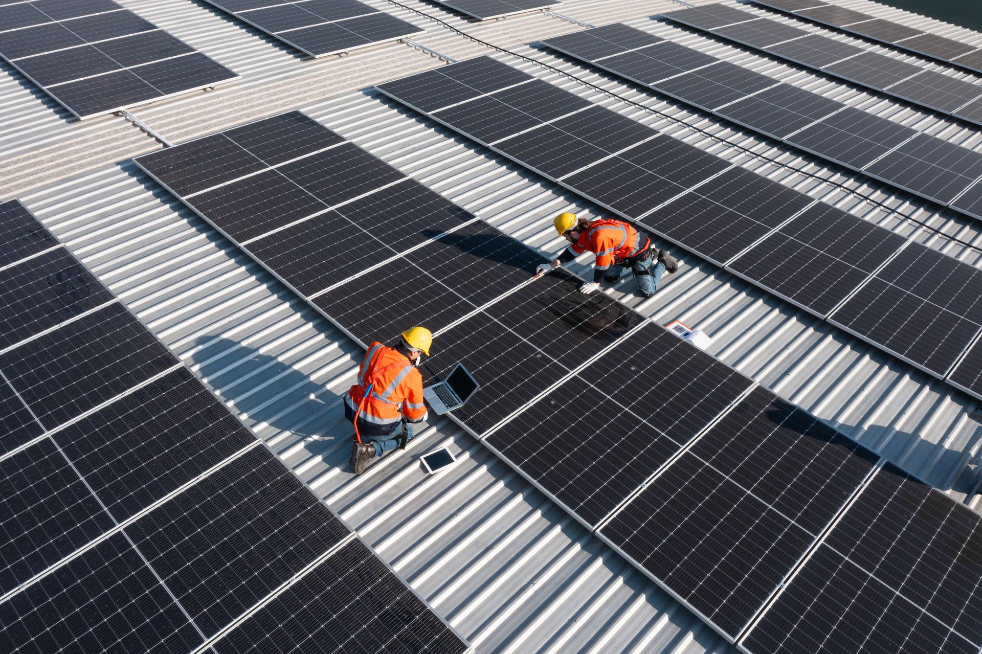 Workers in orange vests installing solar panels on a metal roof Workers in orange vests installing solar panels on a metal roof