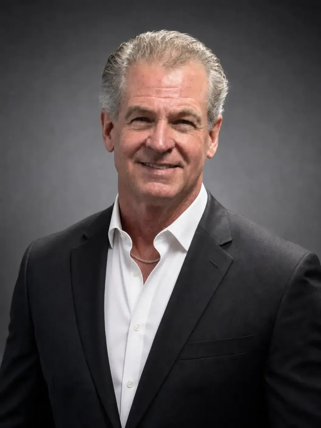 Portrait of a smiling man in a black suit and white shirt against a gray background