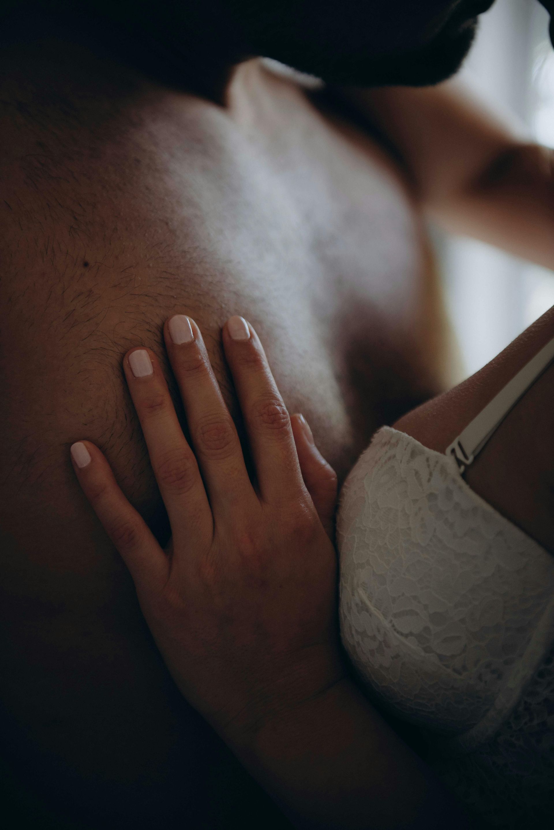 Close-up of a hand resting on a person’s chest beside a white lace bra