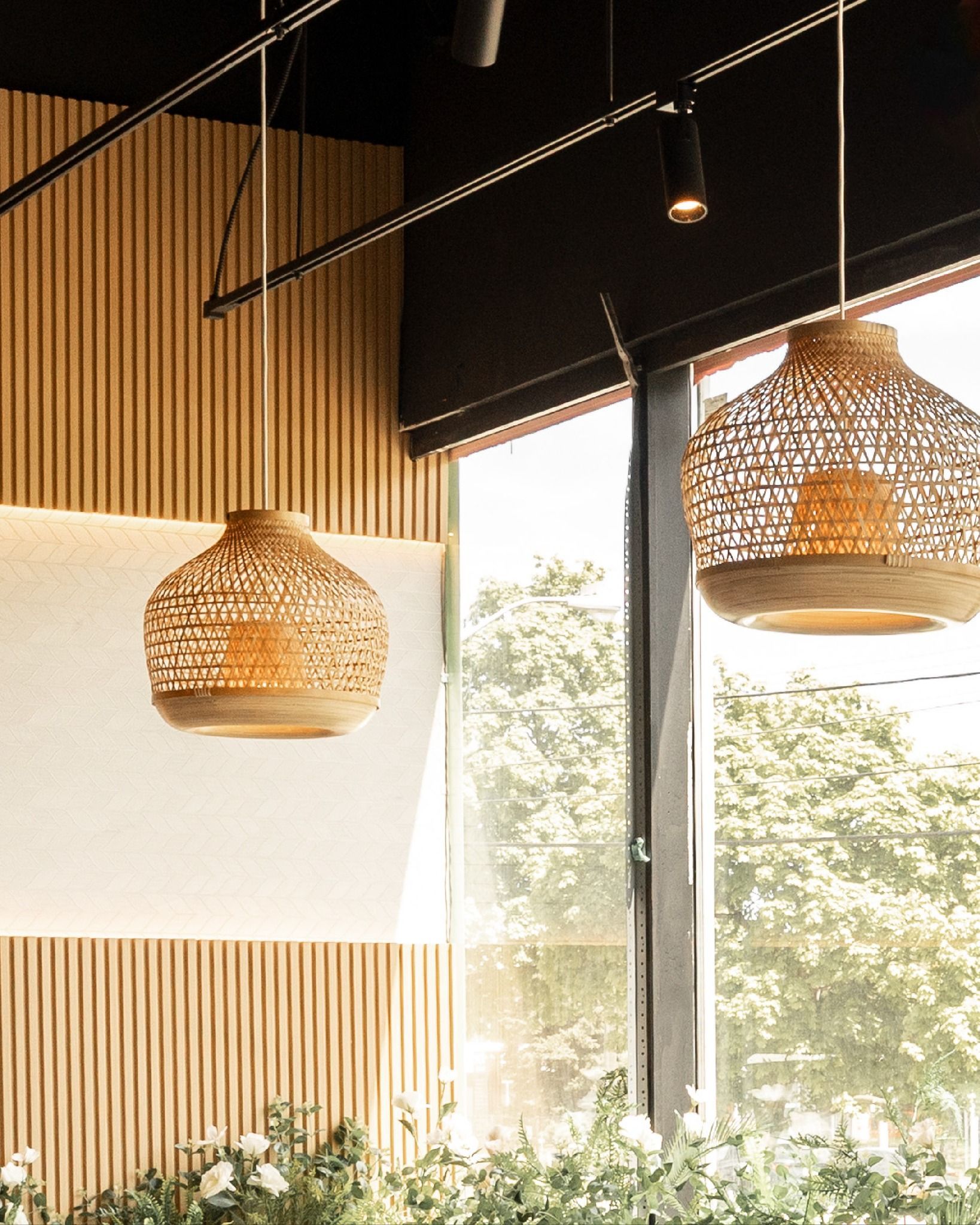 Warm modern interior with woven pendant lights and large windows overlooking greenery