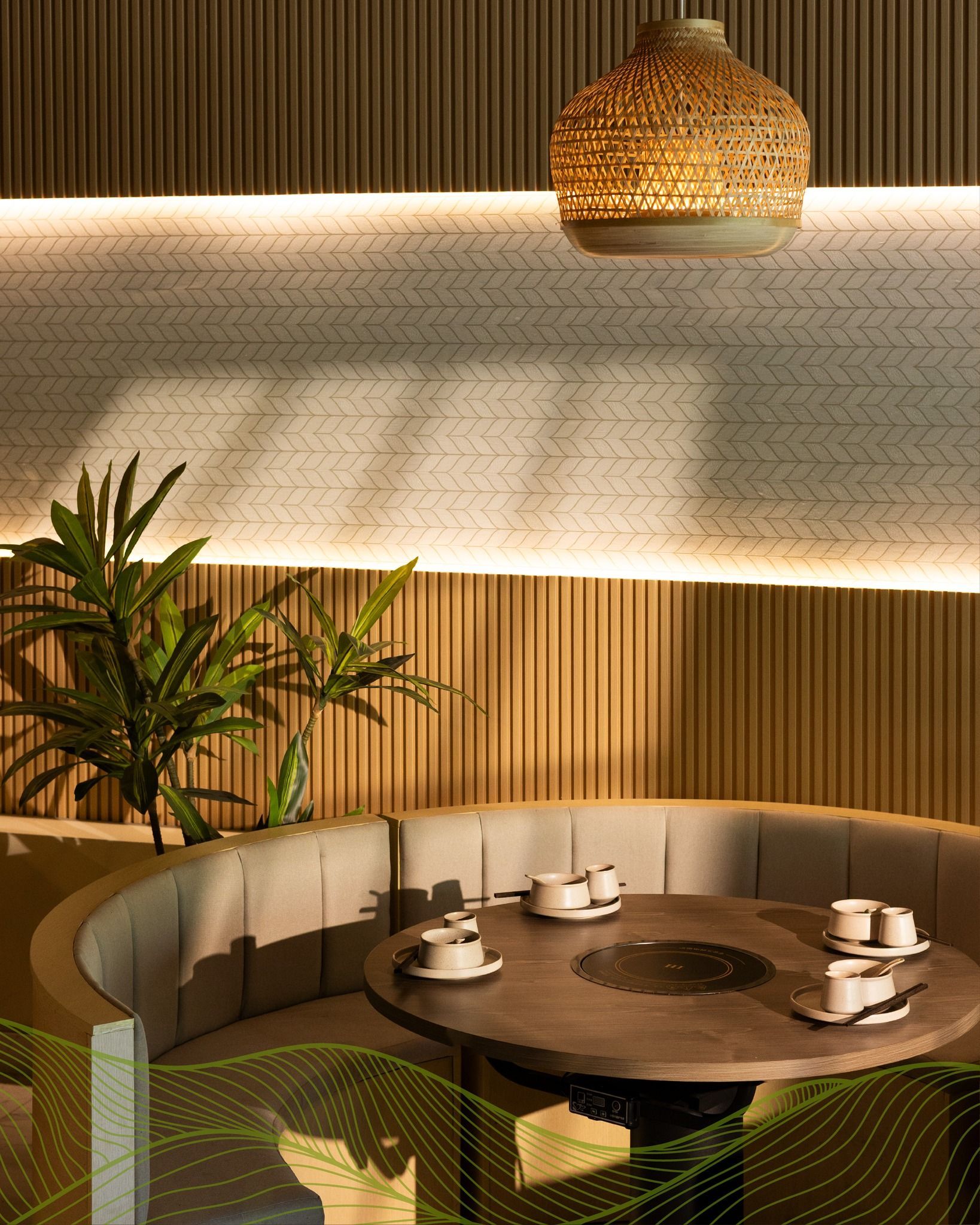 Warm modern restaurant booth with a round table, woven pendant light, and potted plants in soft lighting