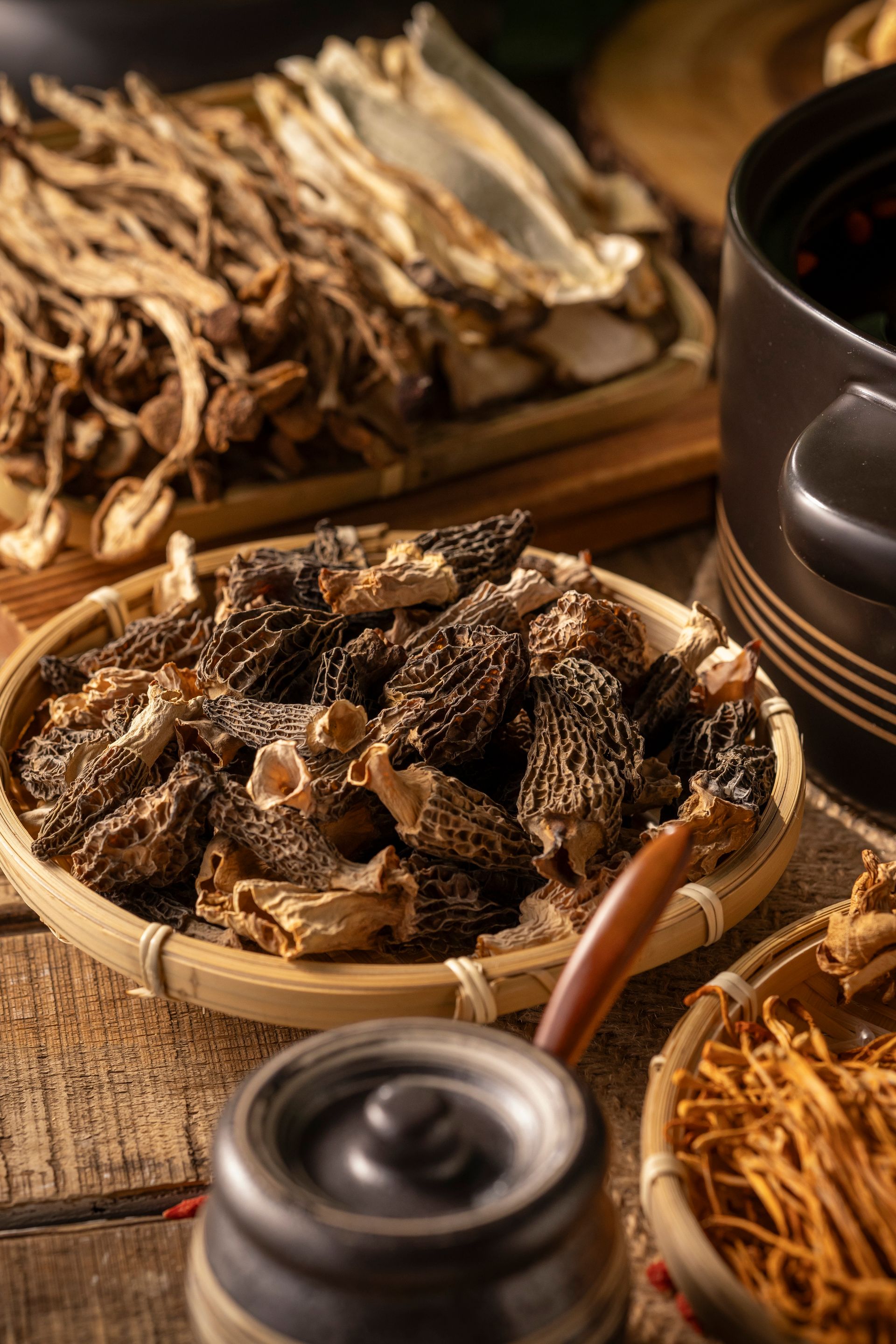 Dried herbs and mushrooms in bowls on a woven mat with chopsticks and tea cups