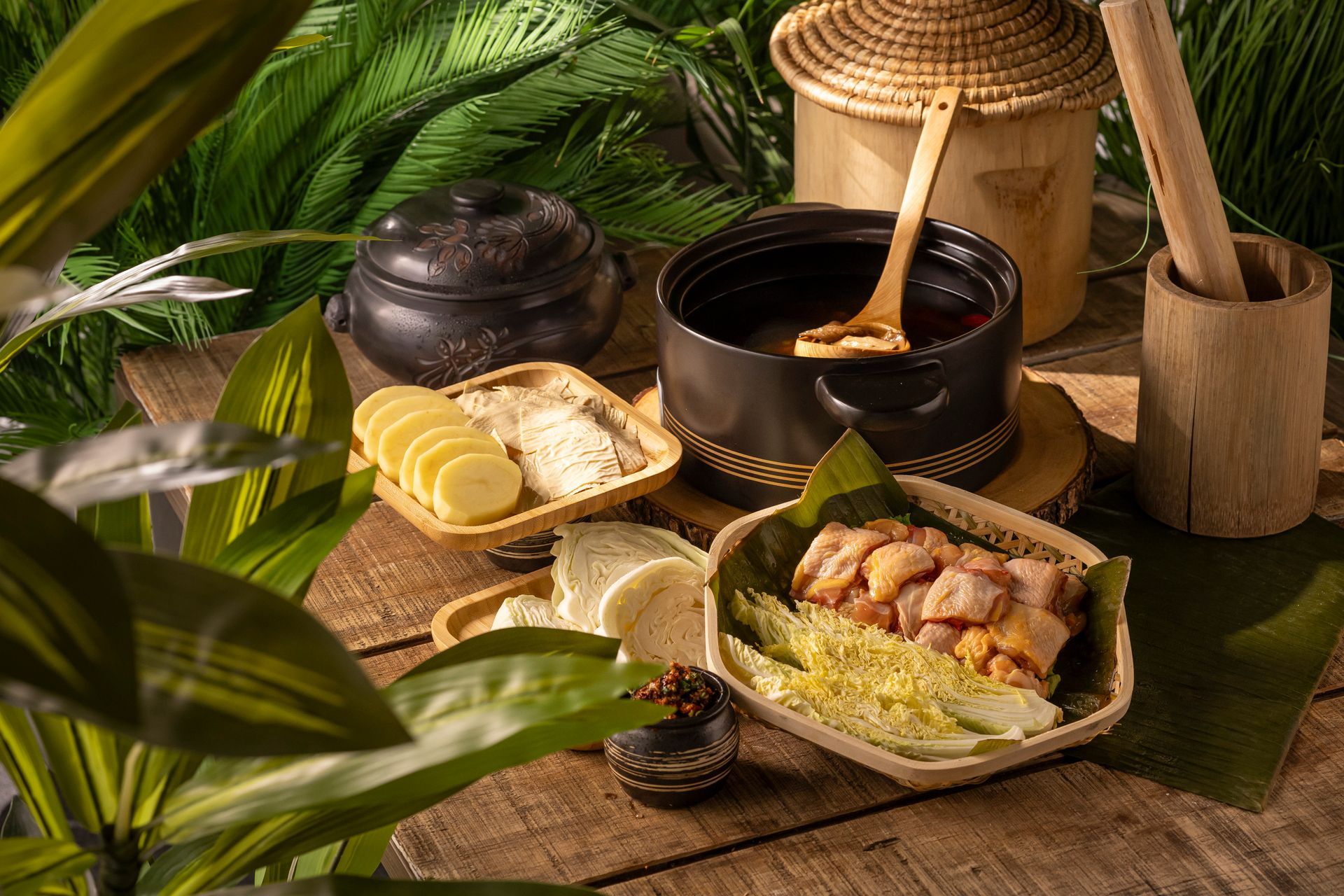Traditional meal served on banana leaves with soup, sliced bread, and drinks amid lush green foliage