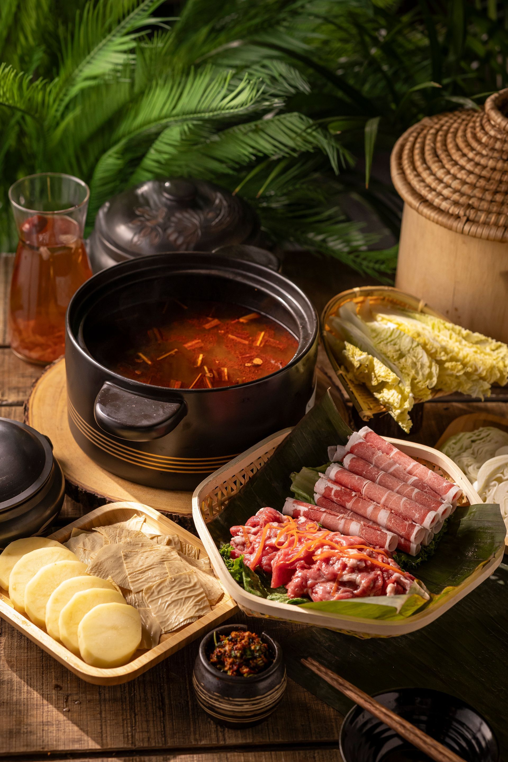 Asian hot pot spread with broth, sliced meats, vegetables, and dipping sauces on a table