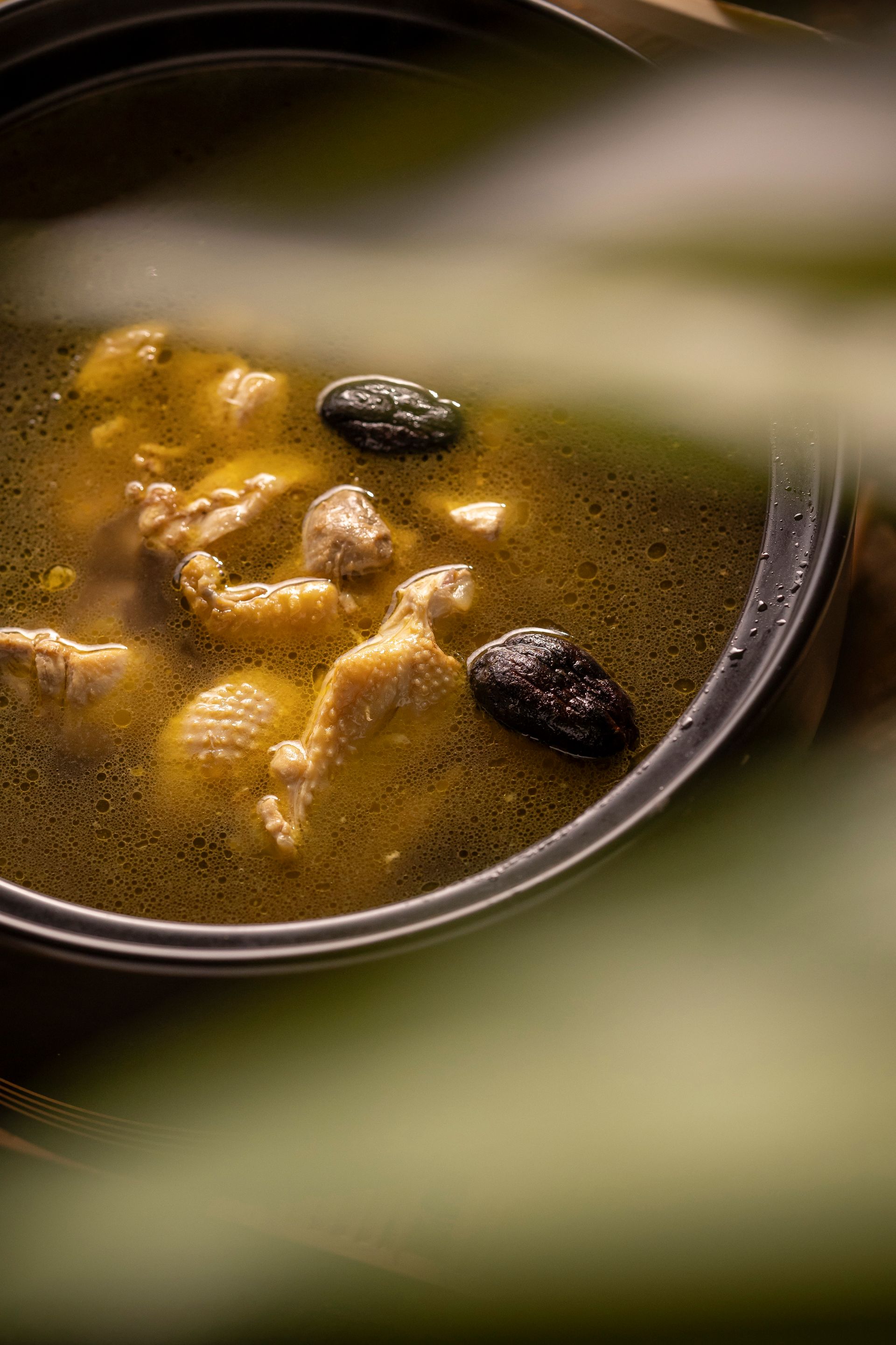 Close-up of a bowl of soup with dumplings, herbs, and two dark garnish pieces
