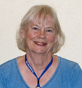 Woman with short blonde hair smiles, wearing a blue shirt and a blue lanyard that says