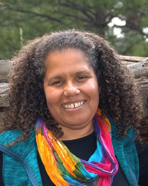 Woman with curly hair, smiling, wearing a colorful scarf, teal jacket, outdoors.