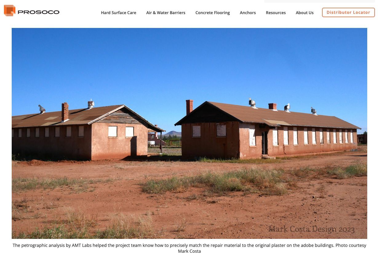 Two brick buildings with brown roofs, set against a blue sky, on red dirt.