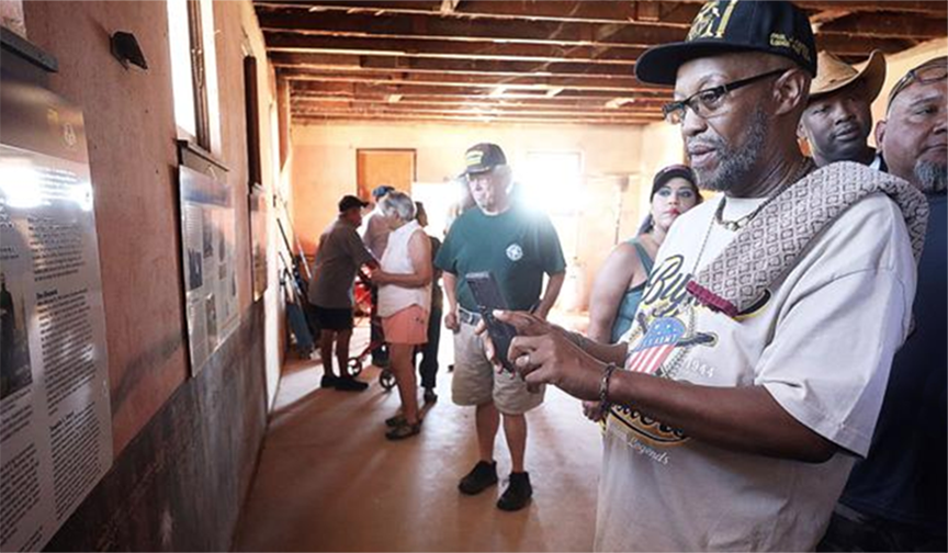 A man in a hat examines photos on a wall, surrounded by other visitors. Inside a building.