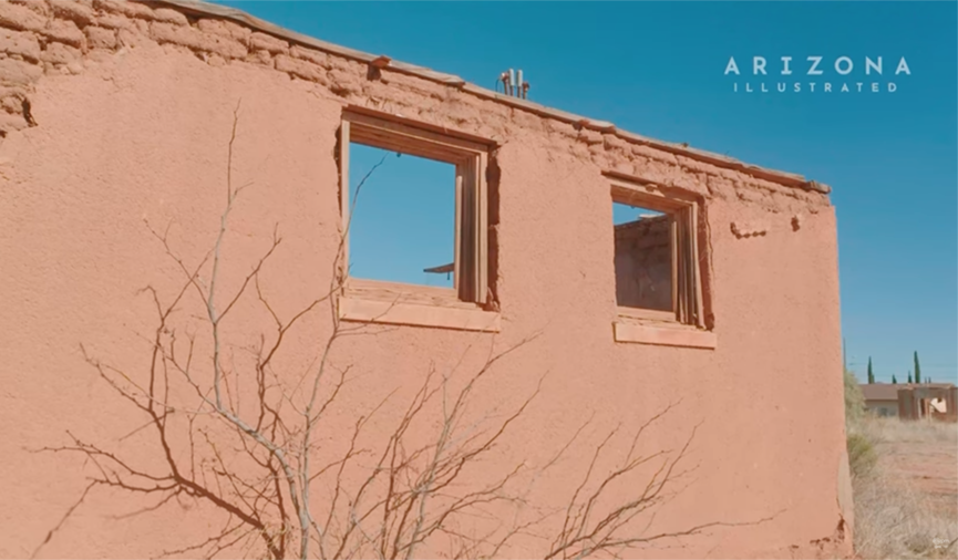 Desert building with empty window frames and faded orange walls under a blue sky.