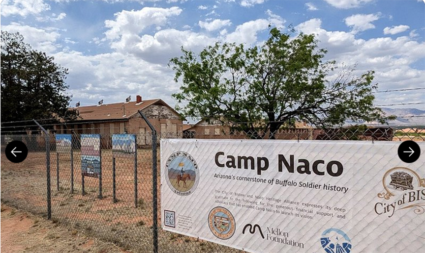 Camp Naco sign and a fenced building under a cloudy sky.