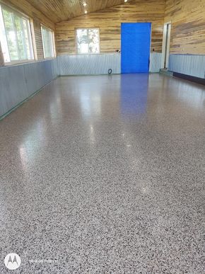 Empty wooden room with gray paneled walls, speckled floor, and a bright blue door at the far end
