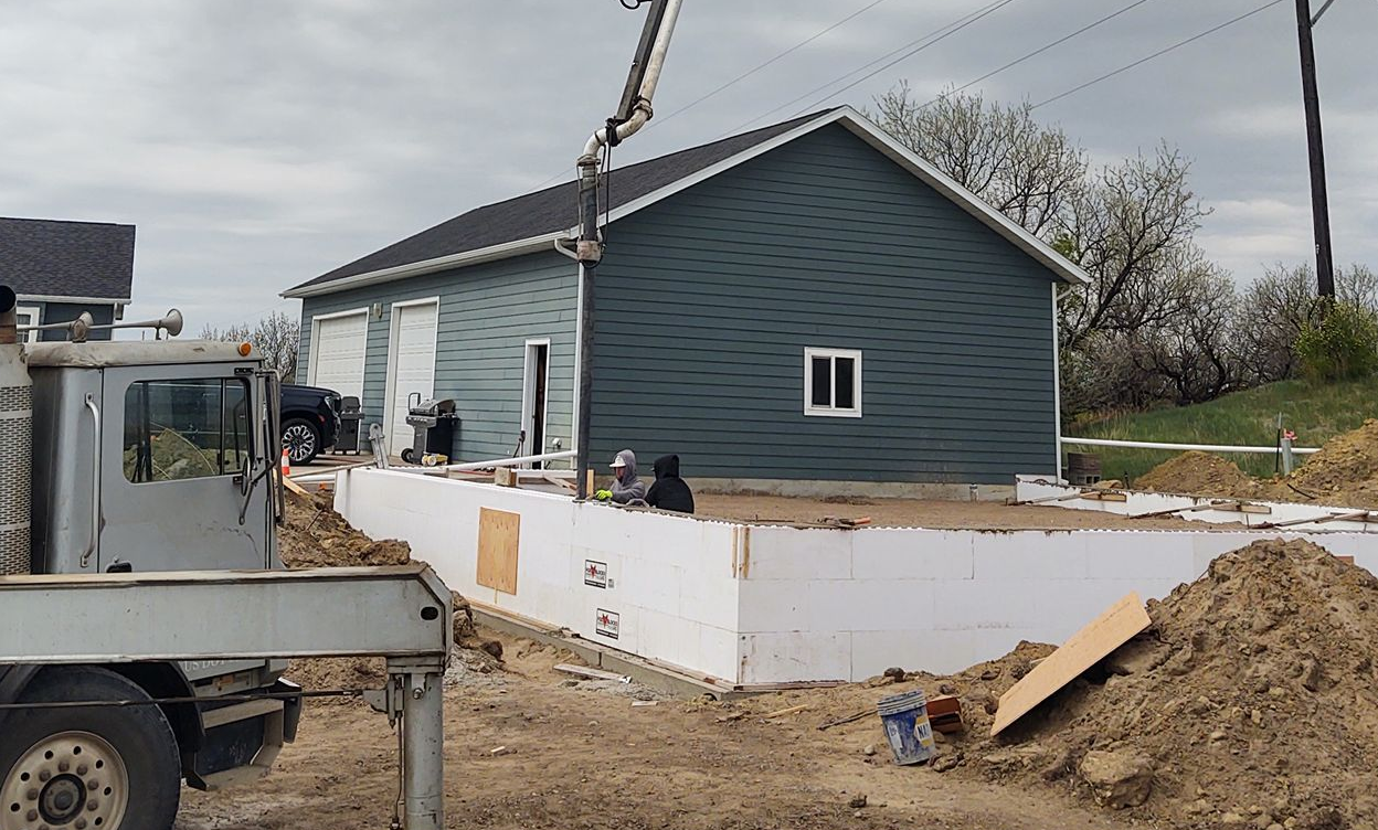 House under construction with white foundation walls, a truck in front, and dirt piles around it