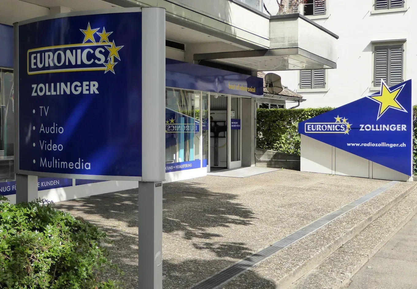 Euronics W. Zollinger Zürich-Geschäftsfront mit blauen Schildern und gläsernem Eingang an einem Kopfsteinpflasterweg