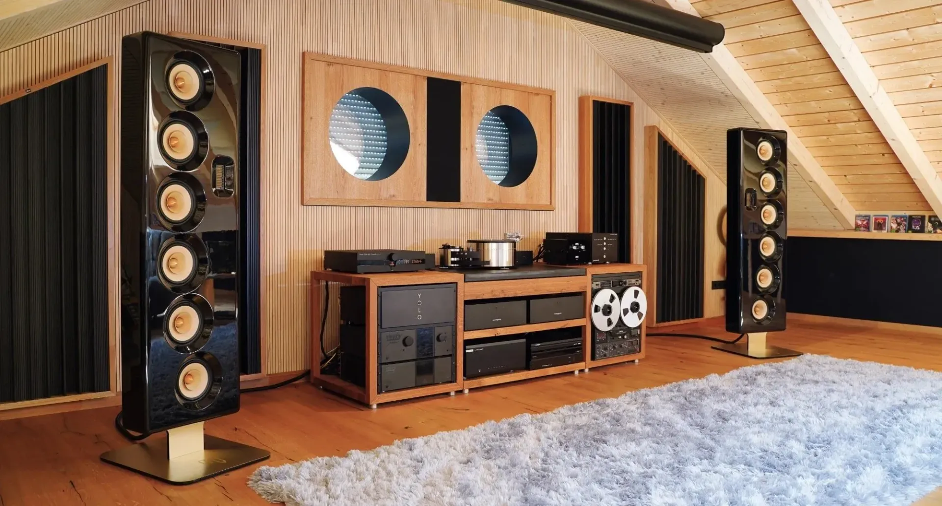 Moderne Stereoanlage mit hohen Lautsprechern in einem gemütlichen, holzgetäfelten Zimmer auf einem hölzernen Medienschrank.