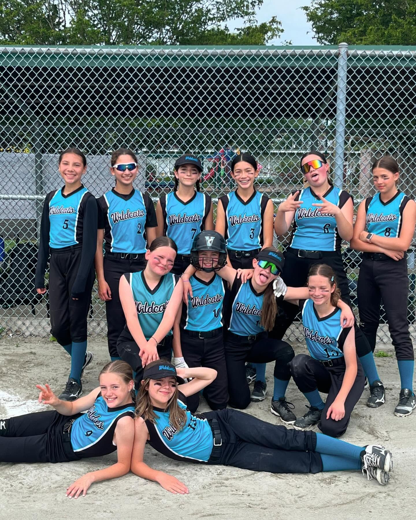 Softball team in blue jerseys posing together on a field in front of a chain-link fence.