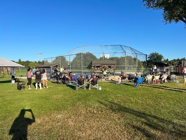 Baseball field with players and spectators under a clear blue sky at a park