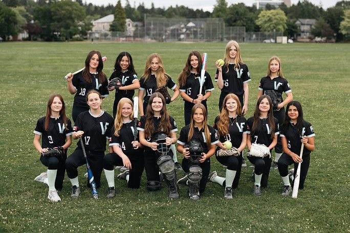 Youth sports team posing in black uniforms on a grassy field, holding sticks with trees in the background