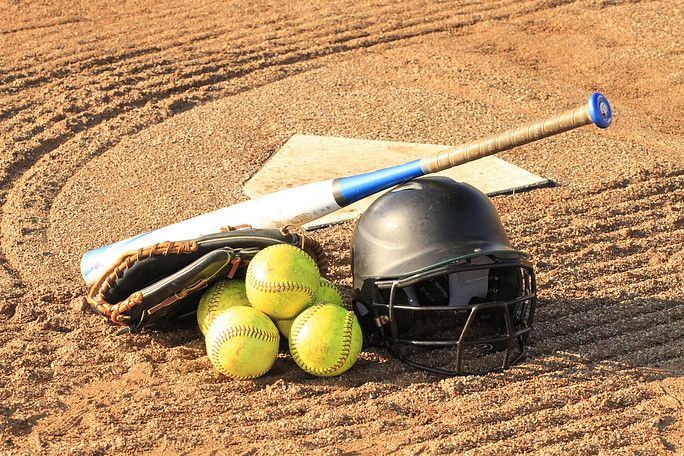 Baseball gear on dirt: bat, glove, balls, helmet, and home plate.