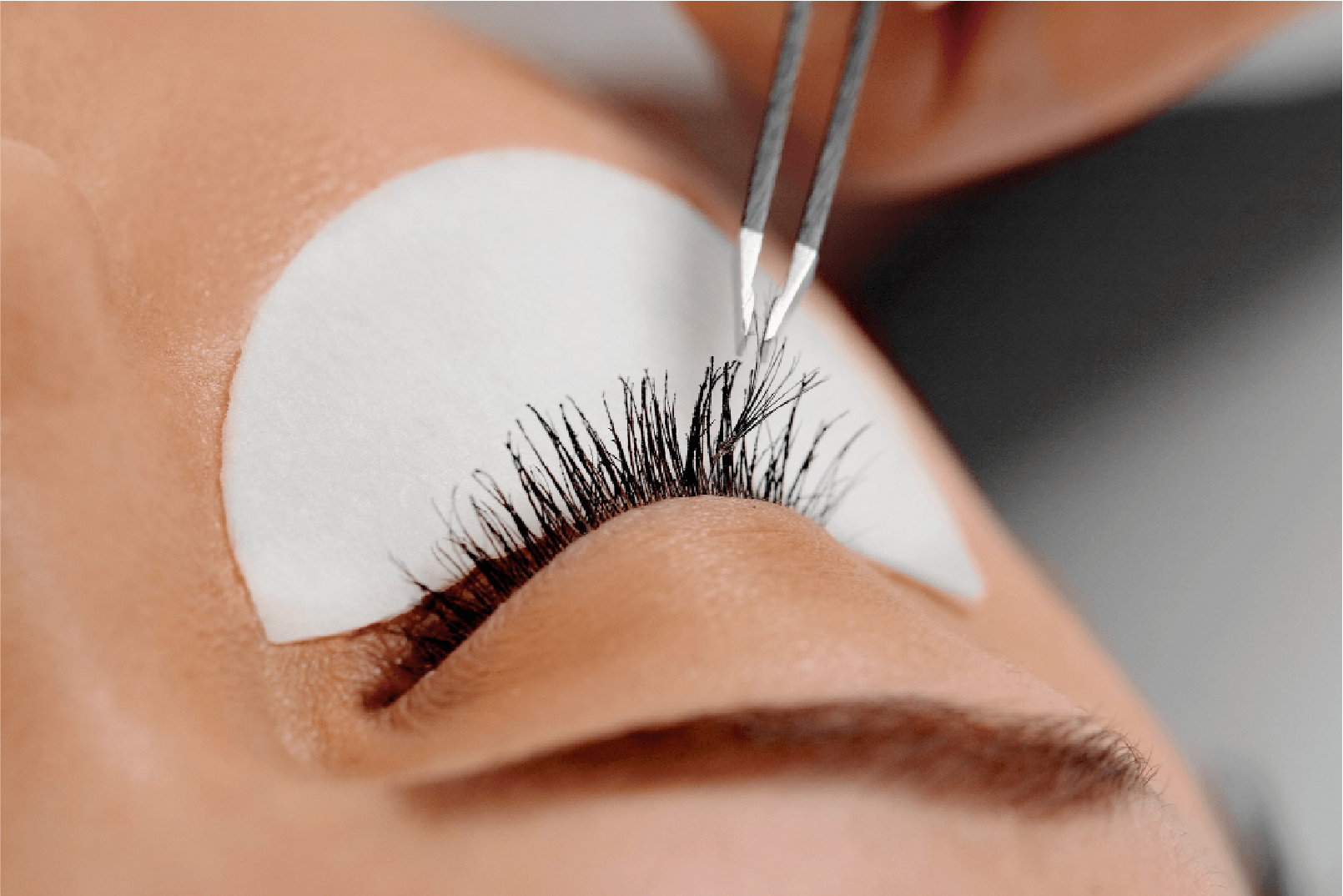 Primer plano del ojo al que se le aplican extensiones de pestañas con pinzas. Parche debajo del ojo colocado.