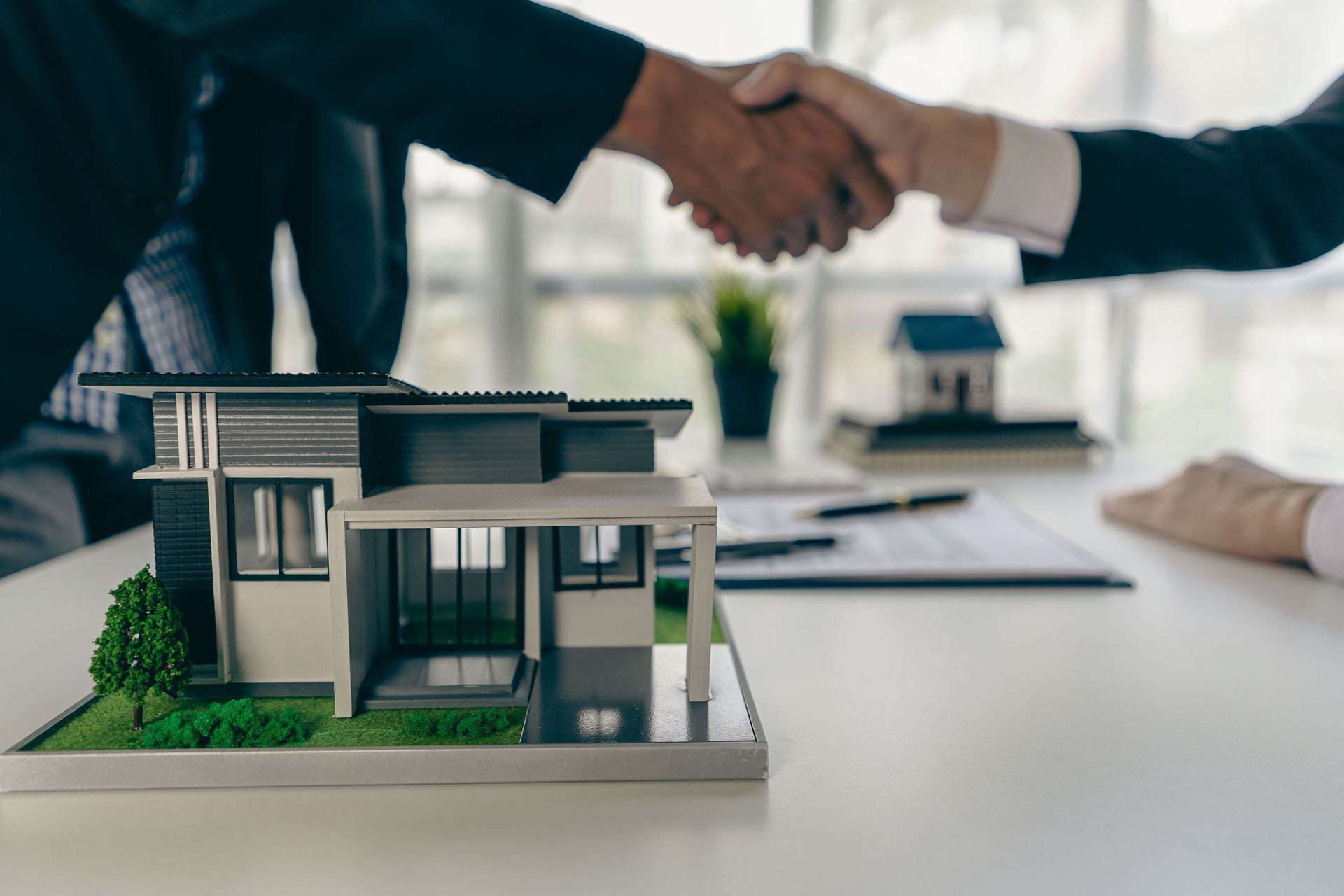Handshake over model house on desk in a real estate meeting