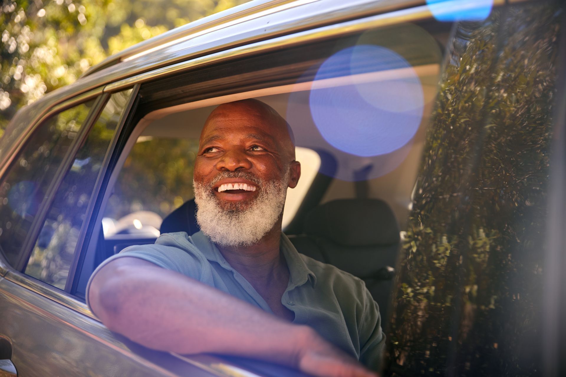 Smiling man sitting in a car with the window open, sunlight streaming in.