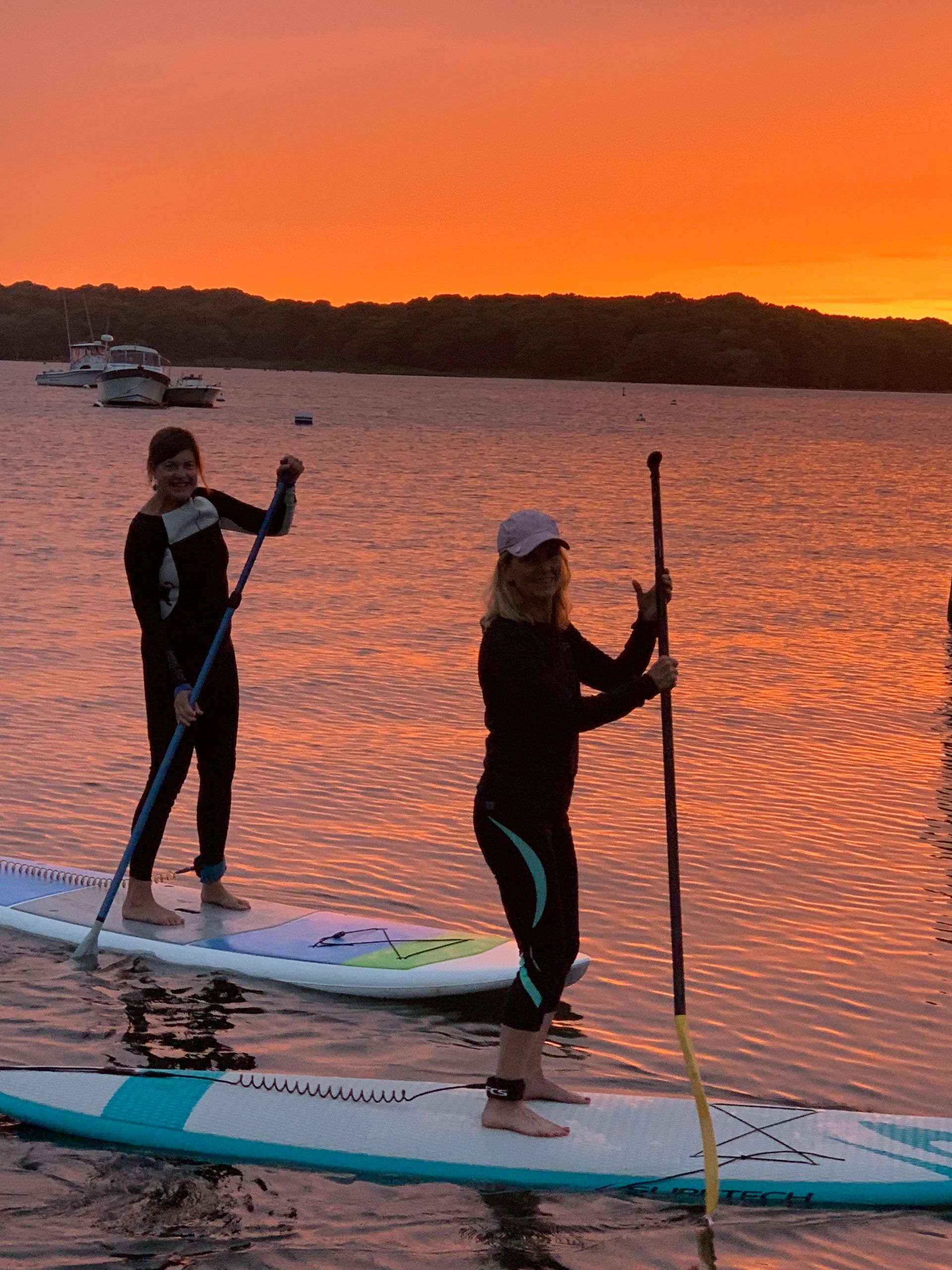 A person riding a paddleboard on calm water with the sun setting